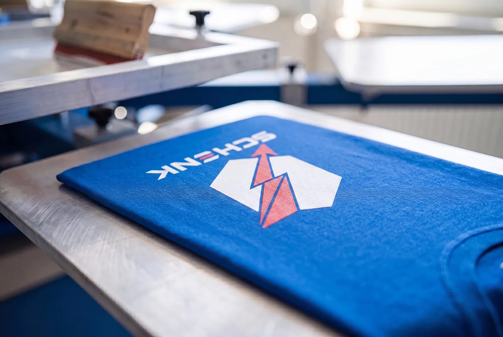 Frisch im Siebdruck bedrucktes blaues Schenk-Shirt auf der Karussell-Druckmaschine – passergenaues Logo als Beweis für Registergenauigkeit